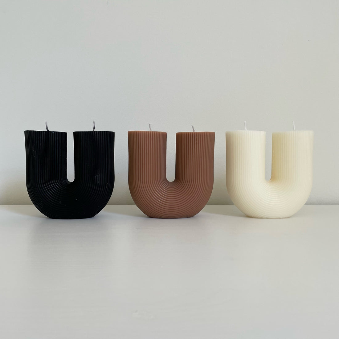 Alt="three Black, brown and ivory white ribbed U-shaped minimalistic candles on a white surface"